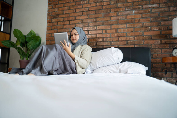 Muslim asian woman using tablet sitting on the bed - Foto, afbeelding