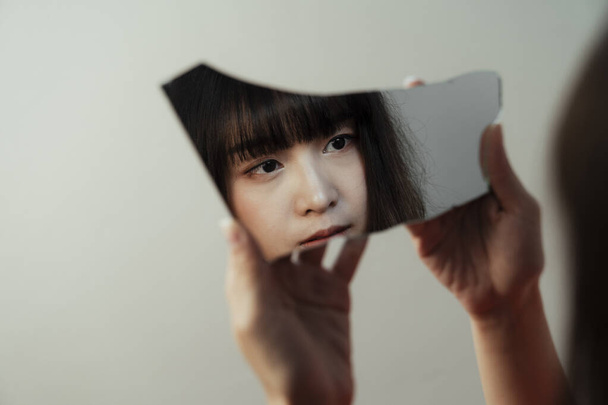 Thai tyttö pitää rikki peili käsissään, mutta hänen heijastus osoittaa, että hänen silmä näky on tyhjä
. - Valokuva, kuva