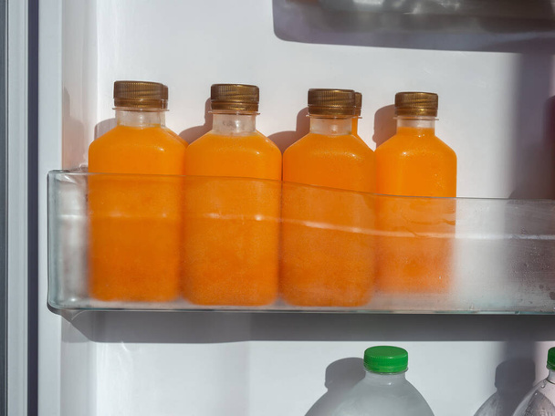Orange juice iced cold in the bottles on shelf in refrigerator. Square shape bottle with cold orange juice. - Photo, Image