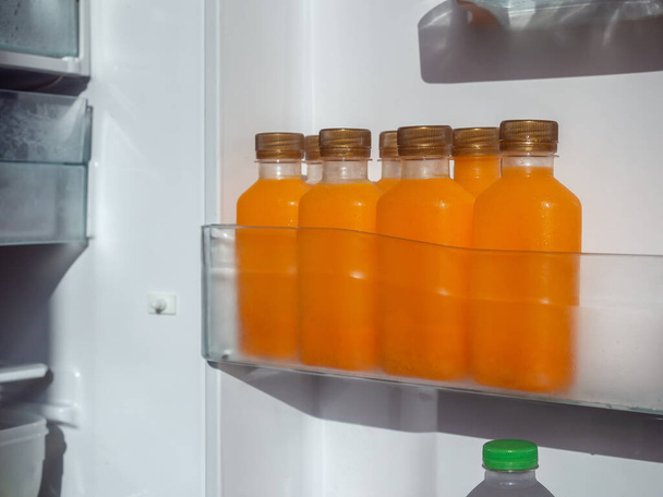 Orange juice iced cold in the bottles on shelf in refrigerator. Square shape bottle with cold orange juice. - Fotó, kép