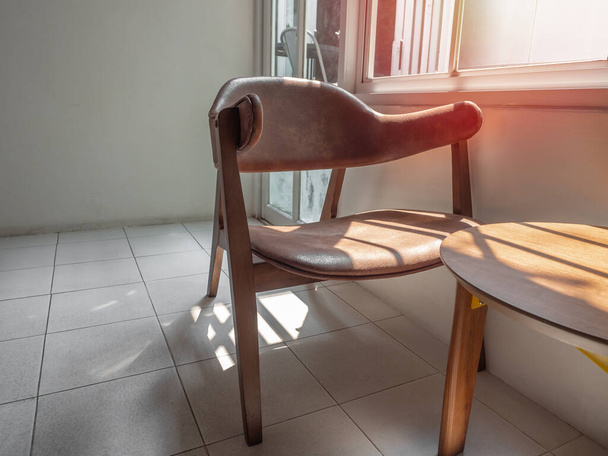 Houten fauteuil retro stijl met bruin lederen zitkussen en houten tafel bij het raam in witte kamer. - Foto, afbeelding