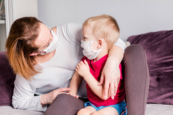 Mom and son in white medical masks look at each other. At home. Horizontal photo - Valokuva, kuva