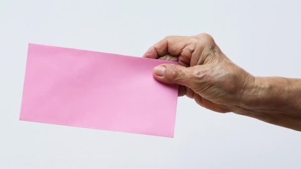Senior vrouw 's rechterhand met roze envelop in geïsoleerde grijze achtergrond, Close-up en macro-shot, Zakelijk concept - Video