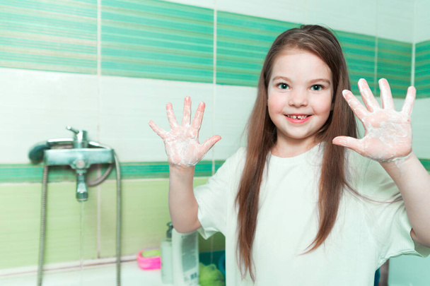 小さな女の子はバスルームで水と石鹸で手を洗う。幸せな子供は石鹸の手のひらを示す。手の衛生とウイルス感染予防。横写真 - 写真・画像