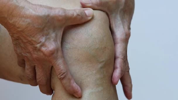 Senior woman suffering from left knee pain, Massaging by her hand in white background, Close up & Macro shot, Asian body skin part, Healthcare, About Massage concept - Footage, Video