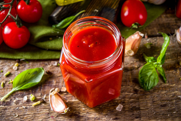 Zelfgemaakte tomatensaus met basilicum, knoflook en verse tomaten. Ketchup, marinara saus in kleine potjes. Op een houten ondergrond, met verse groenten en basilicum. - Foto, afbeelding