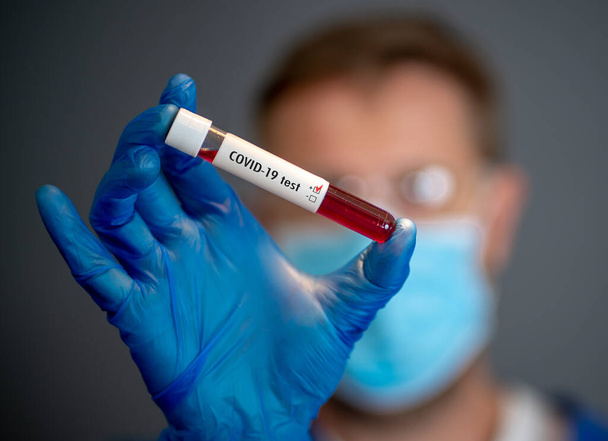 COVID-19. Orvos tudós a személyi védőfelszerelésben, kezében a fertőzött beteg vérmintáját tartalmazó injekciós üveggel a laborban. Coronavirus vérvizsgálat orvosi kezelés és vakcinakutatás céljából. - Fotó, kép