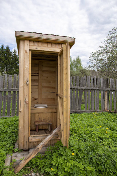 Tradition, hölzerne, rustikale Toilette, WC, mit einem modernen Toilettensitz mit Deckel, im Hof, vor dem Hintergrund eines alten Zaunes. - Foto, Bild