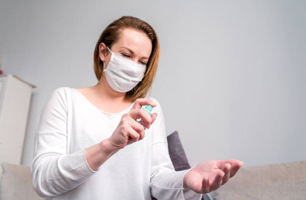 Woman in white medical mask uses antiseptic spray to disinfect hands. Horizontal photo - Fotoğraf, Görsel