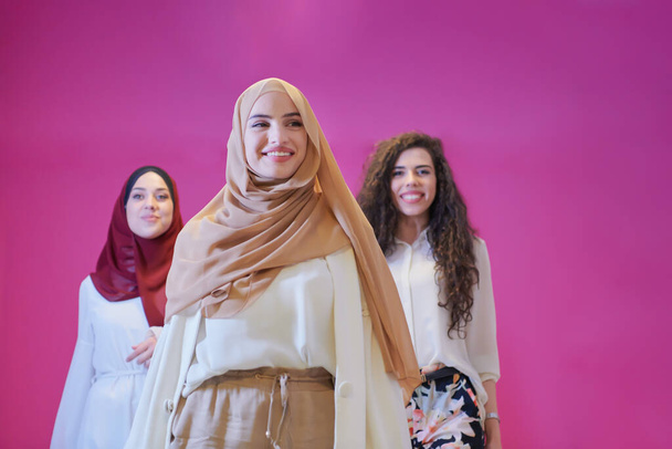 group portrait of beautiful muslim women two of them in fashionable dress with hijab isolated on pink background representing modern islam fashion and ramadan kareem concept - Foto, imagen