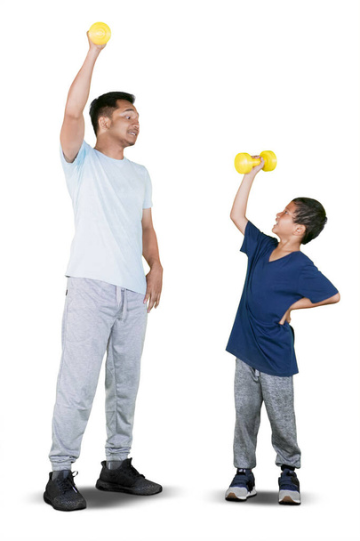 Full length of young father and little son lifting dumbbell while doing workout together, isolated on white background  - Foto, imagen