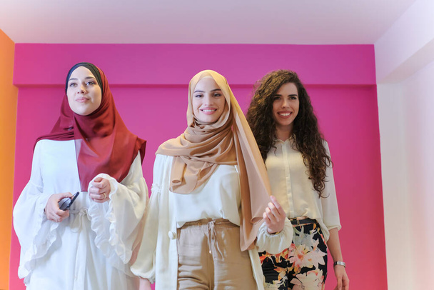 group portrait of beautiful muslim women two of them in fashionable dress with hijab isolated on pink background representing modern islam fashion and ramadan kareem concept - Foto, Imagem