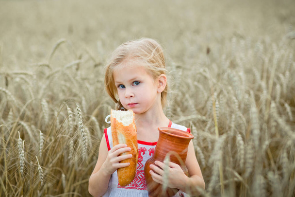 uma criança pequena em um campo de trigo com um jarro de cerâmica de leite
. - Foto, Imagem