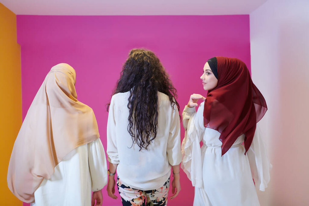 group portrait of beautiful muslim women two of them in fashionable dress with hijab isolated on pink background representing modern islam fashion and ramadan kareem concept - Photo, image