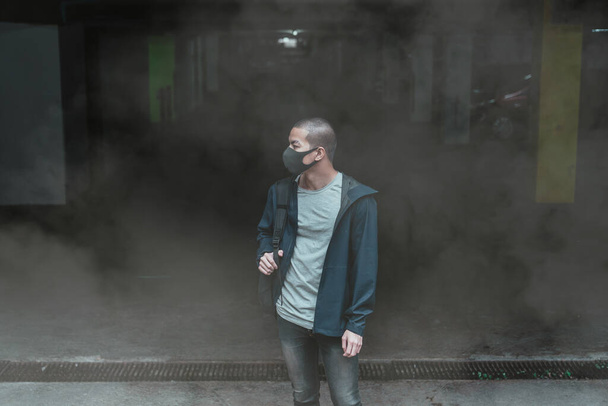 Mann mit echter Anti-Umwelt-, Anti-Smog- und Viren-Gesichtsmaske; dichter Smog in der Luft und in Big Bags, auf dem Parkplatz stehend - Foto, Bild