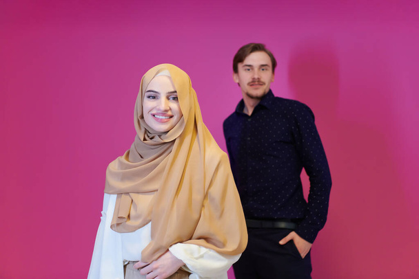 portrait of young muslim couple woman in fashionable dress with hijab isolated on pink background representing modern islam fashion and ramadan kareem concept - Foto, afbeelding