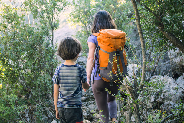 Egy nő sétál a fiával az erdőben, a fiú az anyjával túrázni megy, egy gyerek hátizsákkal a parkban van, gyerekekkel utazik, a gyerek fogja anya kezét, hegyi ösvény, Anyák napja. - Fotó, kép