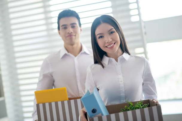 Two coworkers holding boxes with office stuff and looking happy - Fotoğraf, Görsel