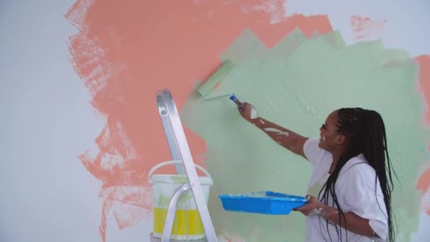 Concetto di ristrutturazione piatto. Sorridente donna afroamericana ridecorare la sua casa in possesso di un rullo di vernice ricoperta di vernice arancione e verde - Filmati, video
