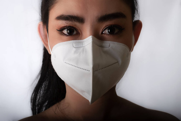 Gri arka planda grip, güvenlik virüsü enfeksiyonu konsepti, gri arka planda PM2.5 toz ve duman gibi hava yoluyla bulaşan solunum hastalıklarından korunmak için 95. tıbbi maske takan genç Asyalı kadını kapatın. - Fotoğraf, Görsel