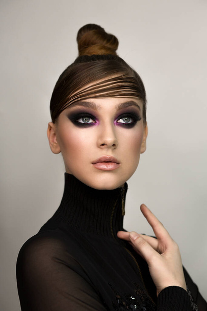 Portrait of a woman. Smoky eyes, black and pink color eyeshadow, makeup. The hair is combed on the forehead. Looking up. A hand touches the neck. Gray background, isolated. - 写真・画像