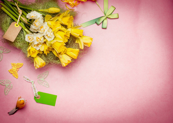 Ramo de flores de saludo de primavera con etiqueta en blanco y decoración. Narciso sobre fondo pastel, borde de vista superior
 - Foto, Imagen