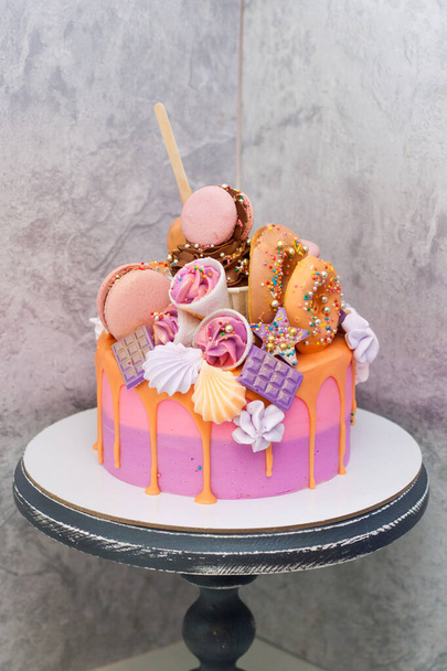 Pink and orange birthday cake decorated with macaroons, meringues, donuts, waffle cones, cake pops and chocolate bars. - 写真・画像