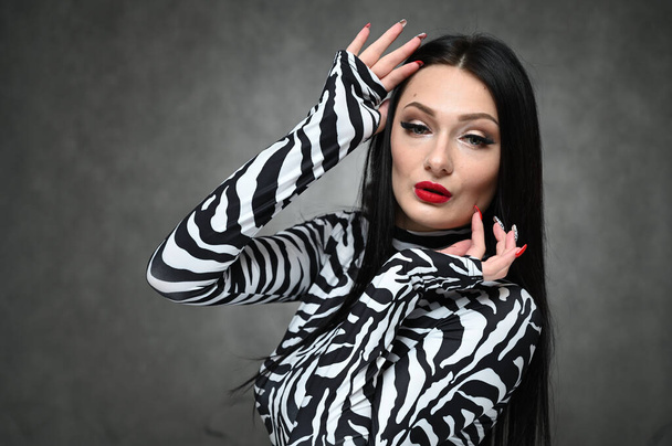 Glamouröses Mädchen in gestreifter Bluse vor grauem Hintergrund im Studio. Ein horizontales Porträt einer modischen kaukasischen Brünette mit hervorragendem Make-up zeigt ihr Gesicht. - Foto, Bild
