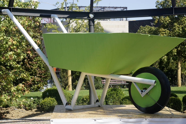 Oversized green, new and empty wheelbarrow use for gardening or construction displayed on a platform. Gardening or construction tool . - Photo, Image