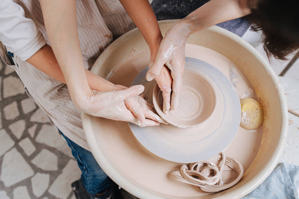 Woman teaching little boy how to shape bowl together on a pottery wheel. Chance to spend time on learning new skills during isolation. Top view. Hands only. - Foto, Bild