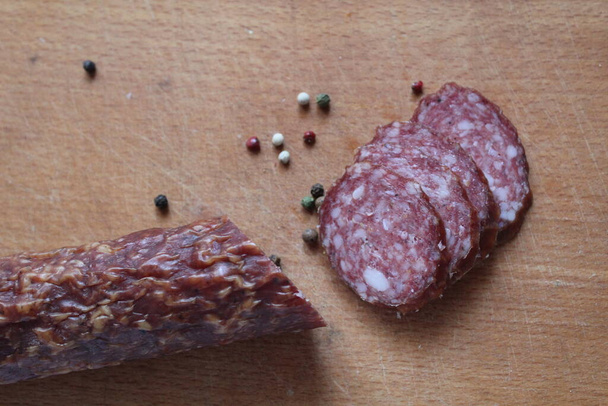 паличка копчена сира ковбаса і нарізані шматочки ковбаси перець білий чорний червоний на дерев'яній обробній дошці
 - Фото, зображення