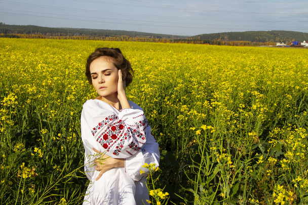 Chica joven con una camisa bordada en un campo de violación amarillo
 - Foto, Imagen