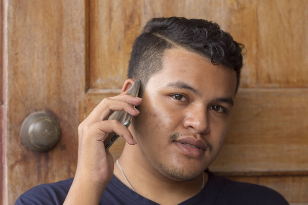 Portret van de jonge Aziatische Thaise man praten over de telefoon en kijken naar de camera - Foto, afbeelding