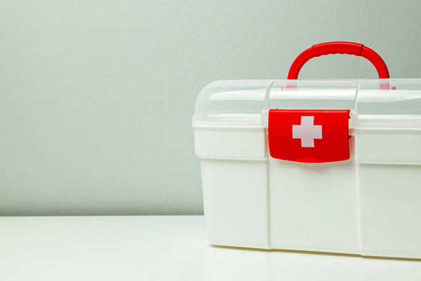 Комплект первой помощи. Белая коробка с крестом и красной застежкой на сером фоне
 - Фото, изображение