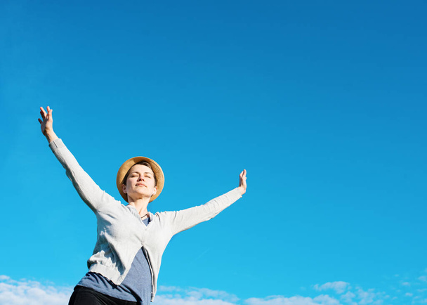 Mujer feliz vistiendo top gris, sombrero de paja, levantó las manos contra el cielo azul
 - Foto, imagen