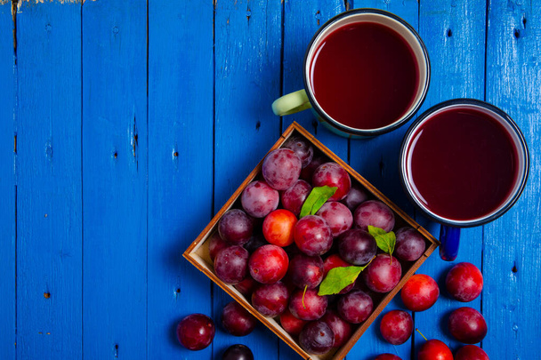 Cup compote plums on blue wooden background - Fotó, kép