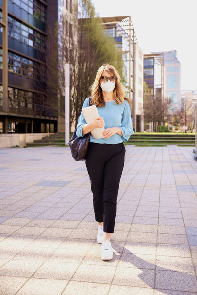 Полный снимок бизнесвумен средних лет в защитной маске на открытом воздухе во время работы
. - Фото, изображение