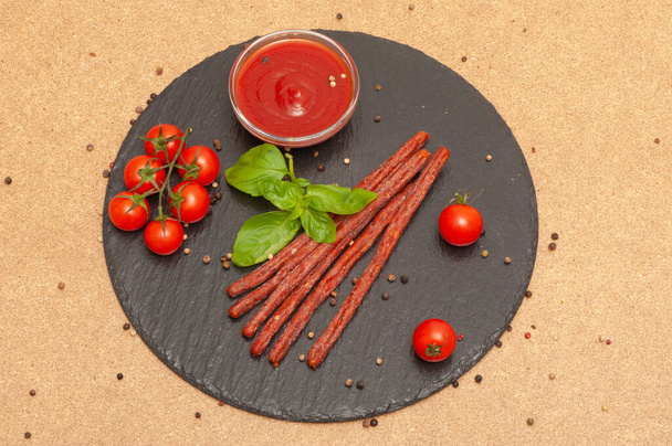 thin long sausage with sauce, cherry tomatoes and basil on a black graphite board - Fotografie, Obrázek