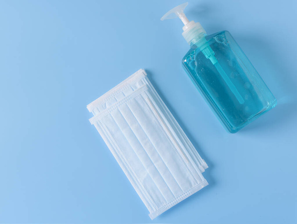 Хирургическая маска для защиты от микробов и гелевого спирта или бутылка дезинфицирующего средства для мытья рук для защиты от коронного циркуля, установленного на синем фоне, плоская
 - Фото, изображение
