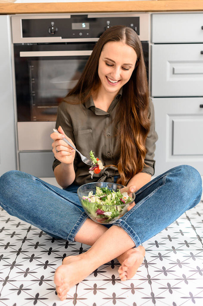 A woman is eating a fresh salad from a bowl - Фото, изображение