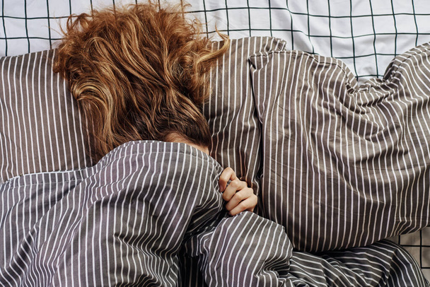 Κοιμωμένη γυναίκα καλυμμένη κάτω από κουβέρτα στο κρεβάτι και παλιό ξυπνητήρι στο μαξιλάρι. Lazy πρωί ana ξυπνήσει έννοια - Φωτογραφία, εικόνα