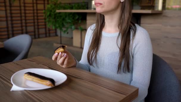 Woman eats chocolate eclair in a cafe - Felvétel, videó