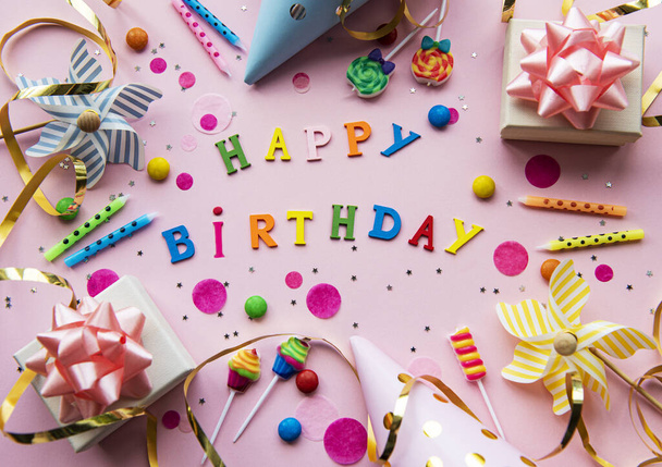 Text Happy Birthday by wooden  letters with birthday asseccories, candles and confetti  on pink background - Фото, изображение