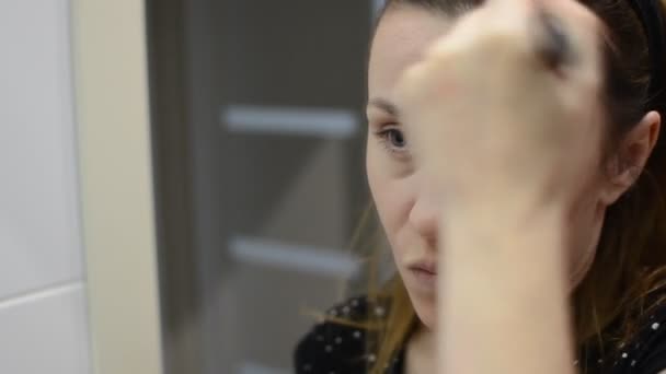 Young woman applies powder on her face with a brush at the mirror - Video, Çekim