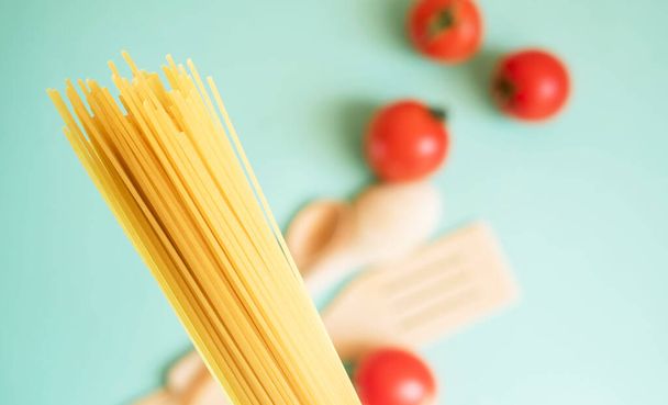 Спагетти на светлом фоне с помидорами, деревянной ложкой / Продукты питания
 - Фото, изображение