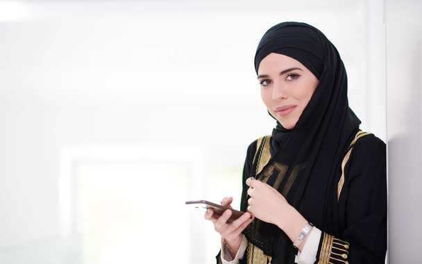 young modern muslim business woman using smartphone wearing traditional hijab clothes at home - Photo, image
