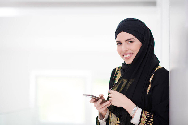 young modern muslim business woman using smartphone wearing traditional hijab clothes at home - Фото, изображение