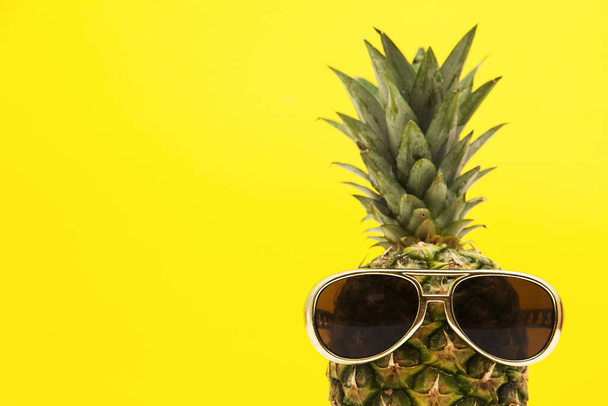 Sommerliche Ananasfrüchte mit Sonnenbrille vor leuchtend gelbem Hintergrund - Foto, Bild