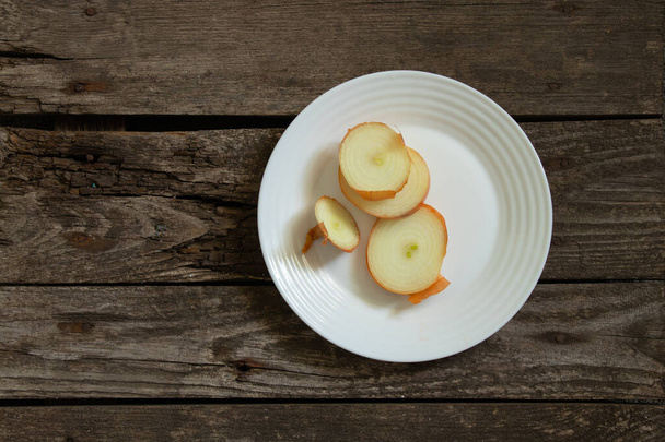 κρεμμύδι βρίσκεται σε ένα λευκό πιάτο σε ένα ξύλινο - Φωτογραφία, εικόνα