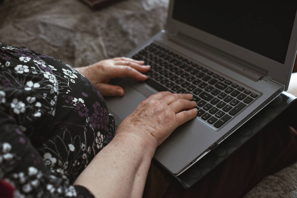 老婦人の美しい手。ノートパソコンで作業するしわのある老婦人の手。年金受給者のための家からの仕事 - 写真・画像